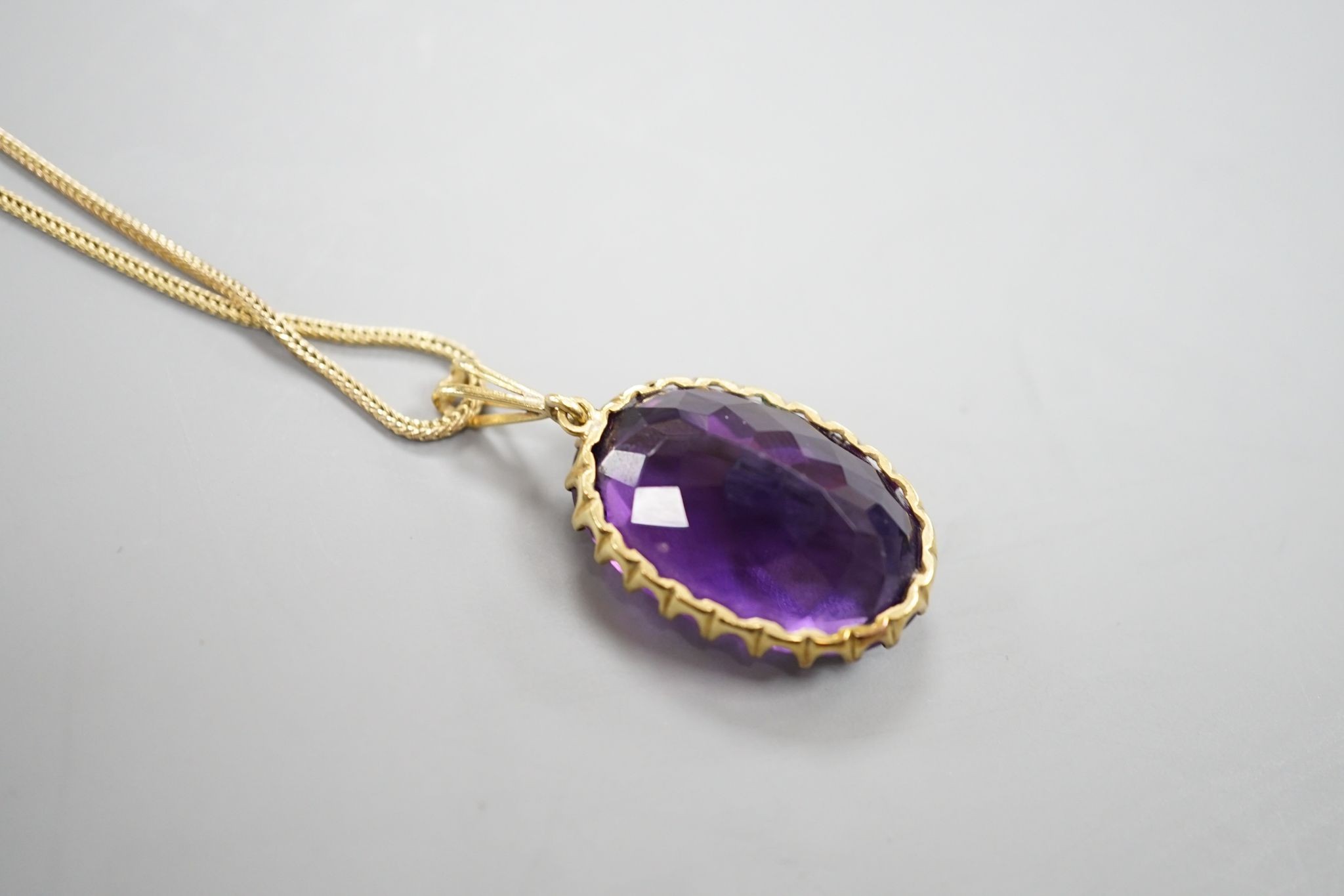 An early 20th century yellow metal mounted oval cut amethyst pendant, overall 37mm, on a yellow metal fine link chain, 49cm, gross weight 10.3 grams.